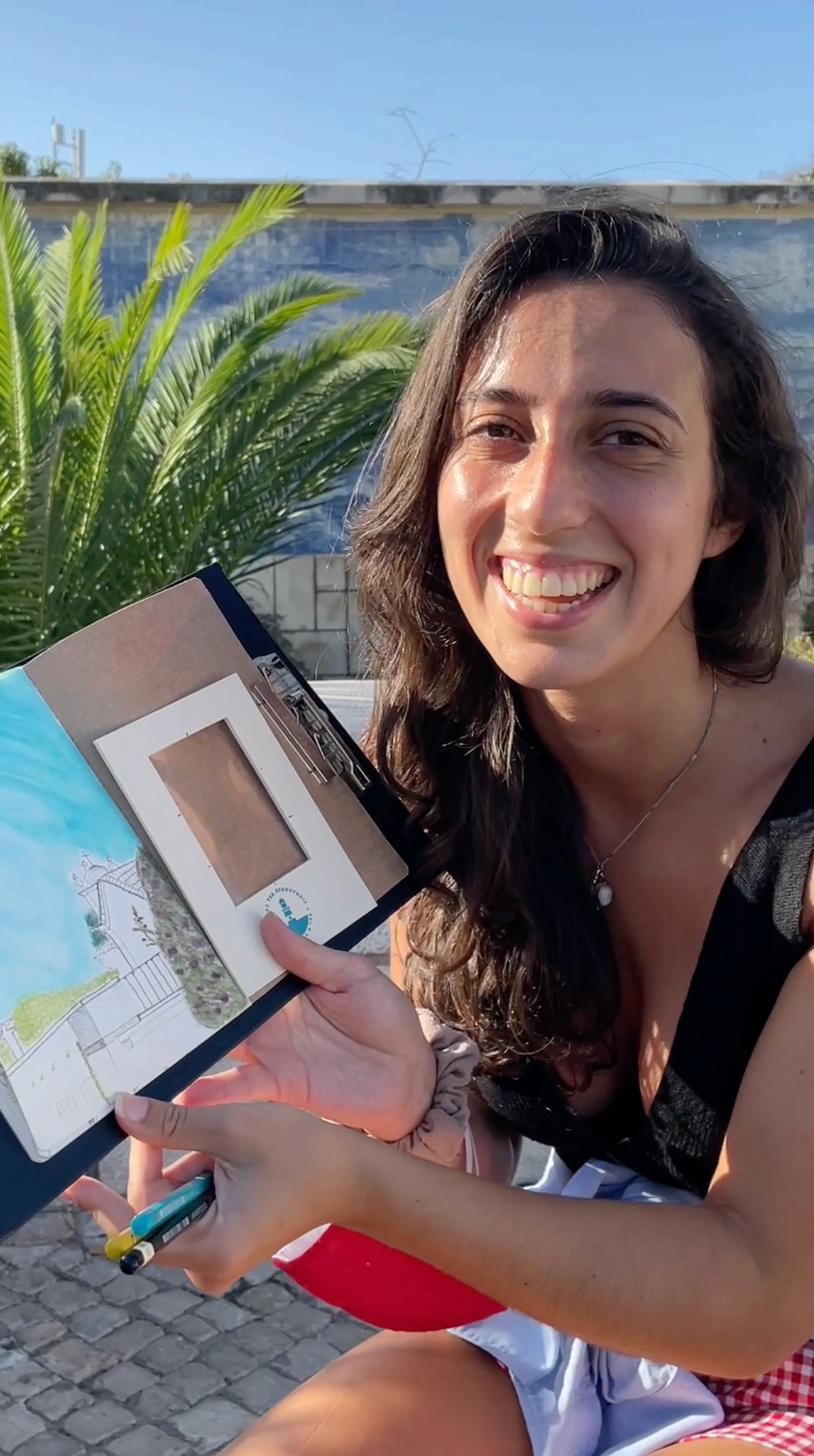 A young woman giving a review after sketching at Miradouro de Santa Luzia in Lisbon, holding a pencil and enjoying the creative process.