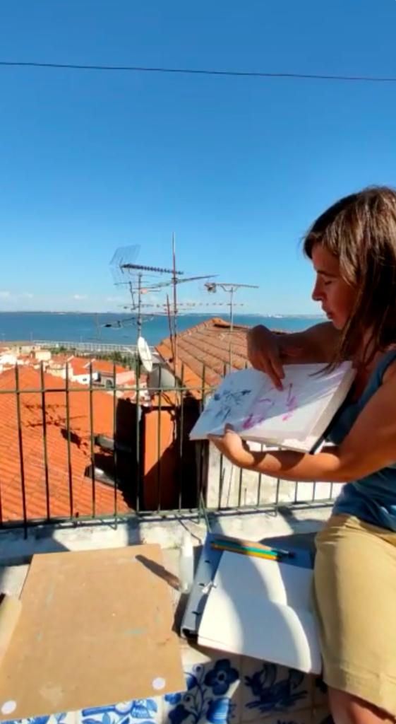 Artist pointing at a sketchbook page during a drawing session at Miradouro de Santa Luzia in Lisbon.